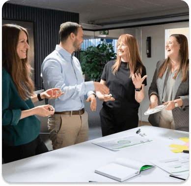 Colleagues laughing in conversation at a workshop table with materials