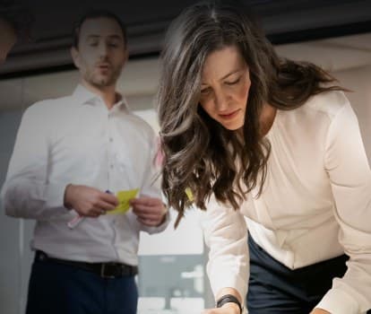 Workshop with sticky notes: a consultant working at the table while a colleague holds up a note for the next process step