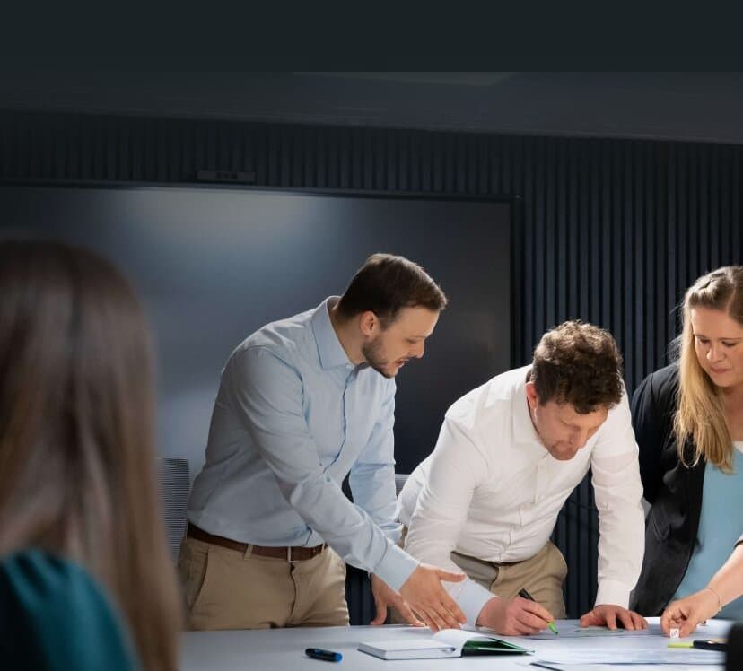 Four colleagues leaning over a table while one of them notes ideas on a large sheet with a marker